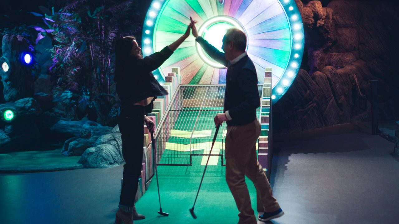 woman and man playing minigolf at tree top, giving high five